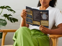 a woman is sitting in a chair reading a brochure